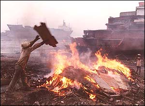 Workers drops boarding onto a fire at Alang