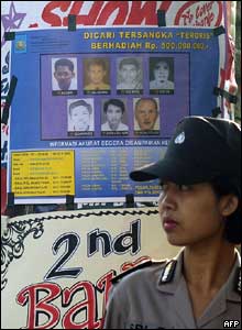 An Indonesian police woman stands in front of a poster of terrorism suspects at the bomb blast site in Kuta