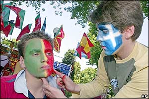A Portugal fan gets his gets face painted by a Greece fan 