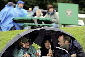 Spectators take shelter under their umbrellas as heavy rain delays the start of play