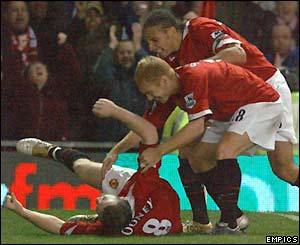 Wayne Rooney rolls on the pitch in delight as Paul Scholes and Rio Ferdinand come to congratulate him