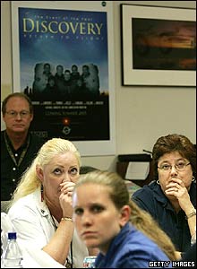 Watching a TV monitor Nasa employees wait for space shuttle Discovery to touch down
