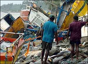Sri Lankan residents stand in front of stranded fishing boats on a shore, 29 December 2004 in Paiyagala, south of the capital Colombo