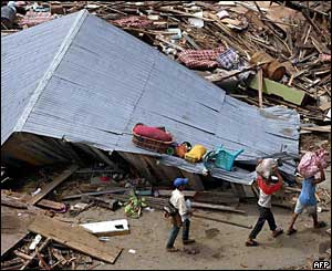 Refugees from Meulaboh, west of Aceh, walk past ruins and a damaged house as they make their way out of town, 31 December 2004. 