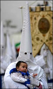 A hooded penitent from the El Resucitado brotherhood carries a baby during a procession in Cordoba