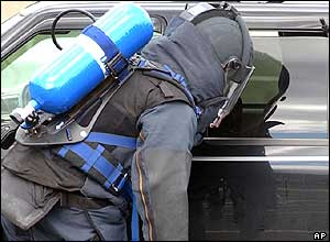 An officer in protective gear inspects a suspect people carrier