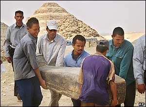 Workers carry decorated mummy with Step Pyramid in the background