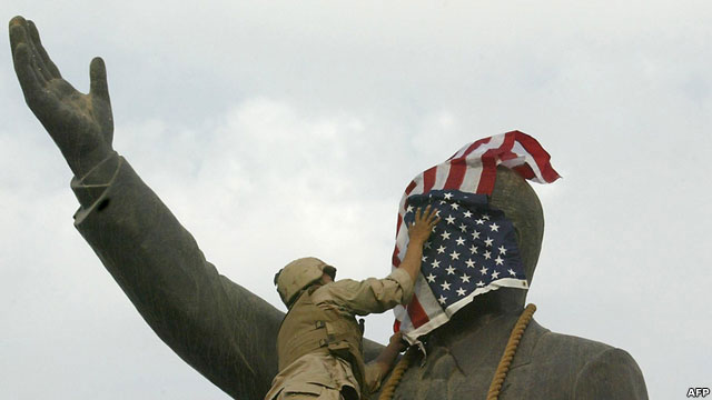 Solider covers a statues face with an American flag