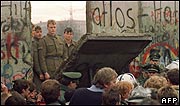 Crowds gather around hole in the Berlin Wall as East German guards look on