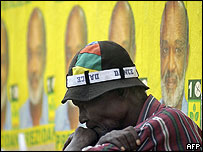 Homem em frente à cartazes de campanha em Porto Príncipe