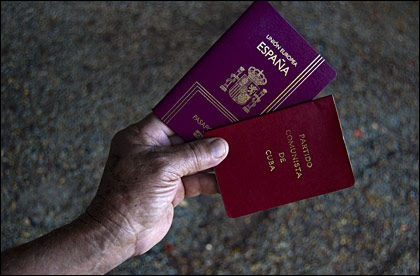 Persona sostiene un pasaporte español y un carnet del Partido Comunista de Cuba