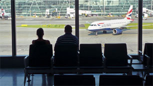 Passengers in an airport terminal, with planes in the background