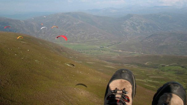 Airborne paraglider's feet in foreground of landscape