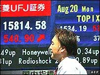 Pedestre passa em frente a um placar eletrônico com indicadores financeiros em Tóquio, nesta segunda-feira