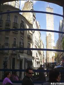 People walk past a shop window reflecting the old downtown of Lisbon 