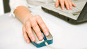 Close-up of a woman's hand using a mouse next to her laptop