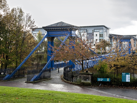 Colour view of St Andrews Suspension Bridge, a pedestian bridge over the River Clyde. In the background stands late-20th Century blocks of flats.