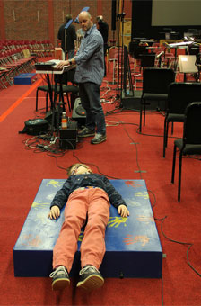 A deaf boy lies on a sound box hooked to a piano