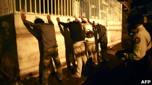 Policiais fazem revista de rotina em jovens em um dos bairros afetados pela violência em Caracas (AFP)