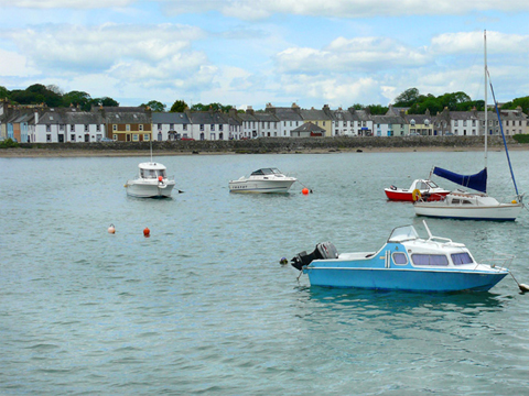 Boats in Garlieston Harbour. A row of single and two-storey buildings line the promenade behind.
