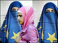 Žena prochází kolem plakátků muslimky zahalůené vlajkou EU