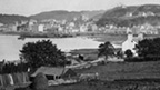 Black and white view of Oban, looking across farmland to the bay, harbour and town.