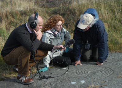 From left to right: Producer Nick Patrick, presenter Vanessa Collingridge and Stan Beckensall discussing one of the cup and ring marks near Fowberry, Woole. Photo courtesy of Dr Aron Mazel