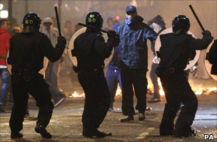 Riot police raise their batons
