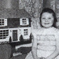 Ruth aged 7 years old, beside a dolls house which her father had made for her as a Christmas present. The dress she is wearing was made by her mother