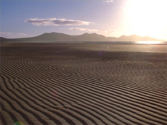 Traeth tonnog Dinas Dinlle a mynyddoedd yn y cefndir