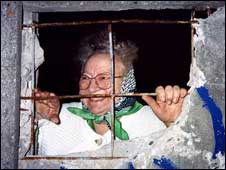An elderly lady looks through a hole in the Berlin Wall