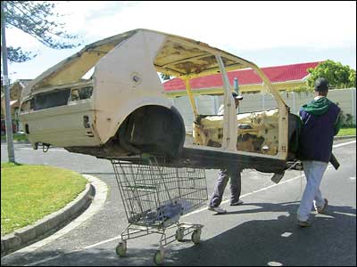 A car's chassis being wheeled along a road on a shopping trolley