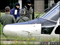 Un ofiţer mascat duce un suspect (cel în albastru) la elicopter