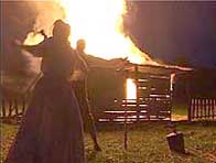 Photograph from a historical reconstruction, two figures stand in front of a burning house