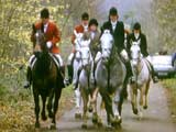 Mounted huntsmen in traditional red jackets riding along a track