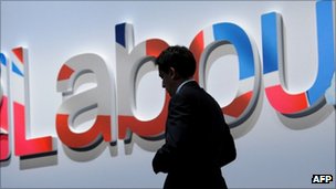 Ed Miliband in the shadows in front of a Labour sign