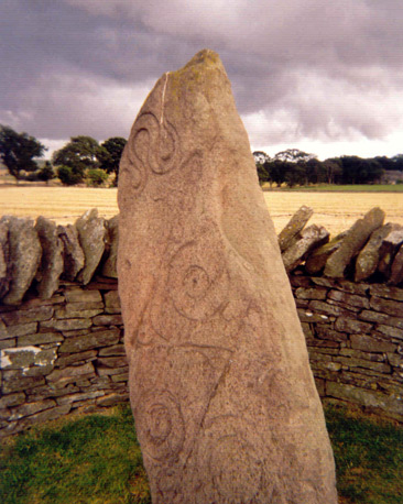 A carved standing stone next to a field of corn