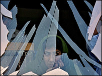 يک زن افغان، از پشت شيشه ای که در اثر انفجار شکسته است، بيرون را می نگرد