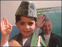 يک کودک افغان در کنار پوستر حامد کرزی 
