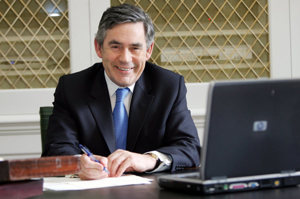 Gordon Brown looking pleased with himself next to a laptop.