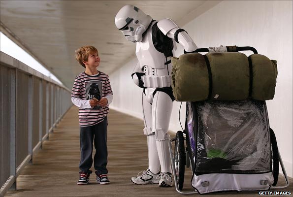 Man dressed as Stormtrooper - and pushing laden luggage trolley - talks to small boy