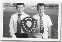 Dau aelod yn dal y darian ac yn gwisgo teis eu clybiau rygbi.