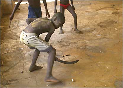 Using a giant seed pod as a hockey stick, a barefoot player strikes the puck in a warehouse abandoned during the war