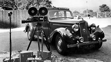 Photograph of a film camera and a 1950s car