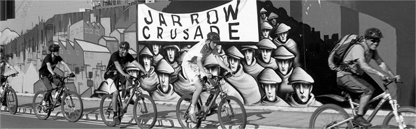 Cyclists speed past a mural of the Jarrow marchers