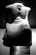 Abstract, gently curving carving of seated male torso and arms, the head broken off