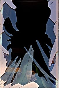 يک زن افغان، از پشت شيشه ای که در اثر انفجار شکسته است، بيرون را می نگرد