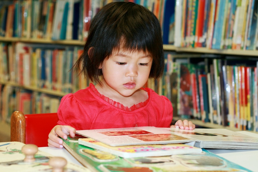 little girl reading book in library @ ying - fotolia