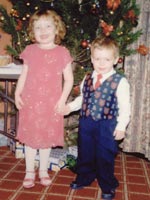 Boy and girl wearing smart clothes in front of a decorated Christmas tree