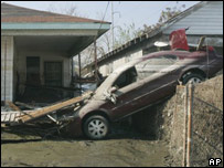 Carro destruído em área com lama após a retirada da água das enchentes